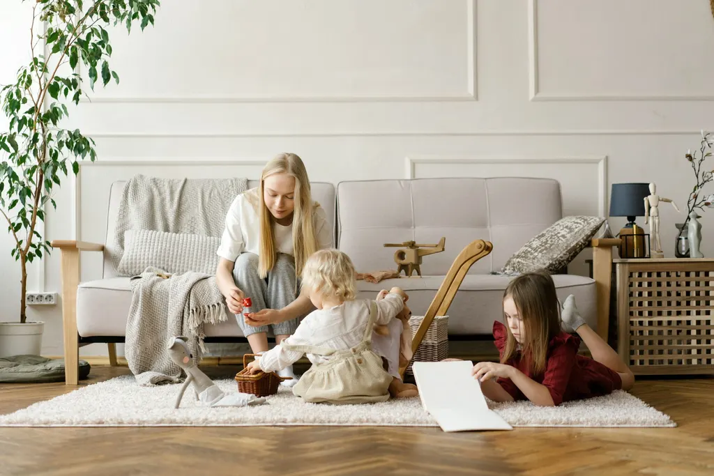 A mother and her two children playing with toys and books on the floor of a bright living room