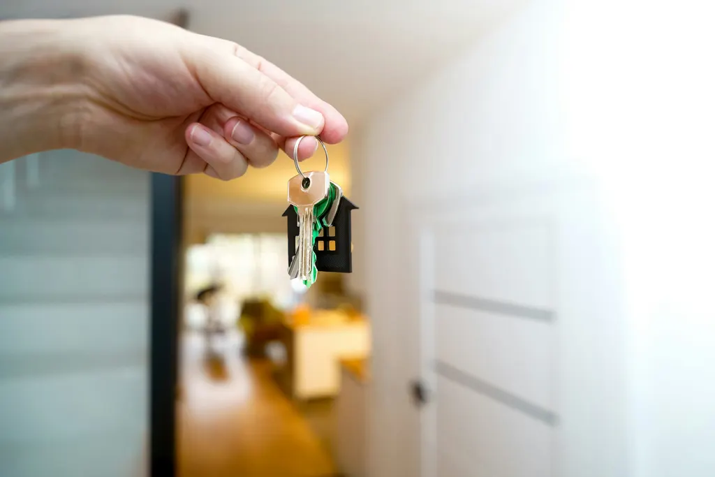 A hand holding a set of house keys in front of a front door